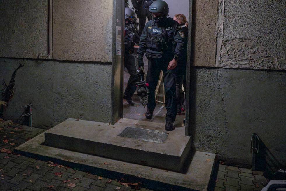 Police officers leave a house during a raid in the early hours of the morning in Munich, German ...