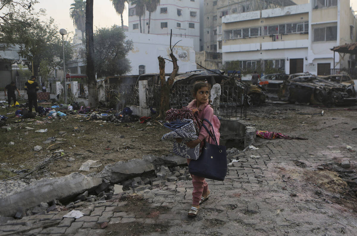 A girl carries blankets as she walks past the site of a deadly explosion at al-Ahli Hospital in ...