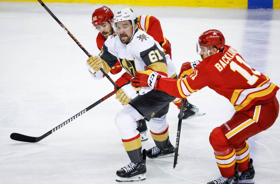 Vegas Golden Knights forward Mark Stone, center, is checked by Calgary Flames defenseman MacKen ...