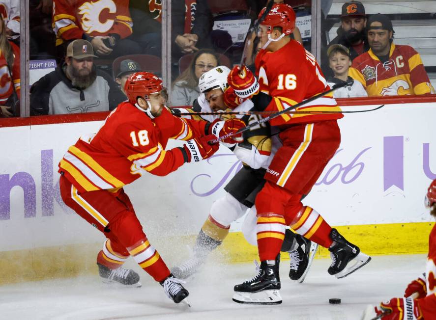 Vegas Golden Knights forward William Carrier, center, is checked by Calgary Flames forward A.J. ...