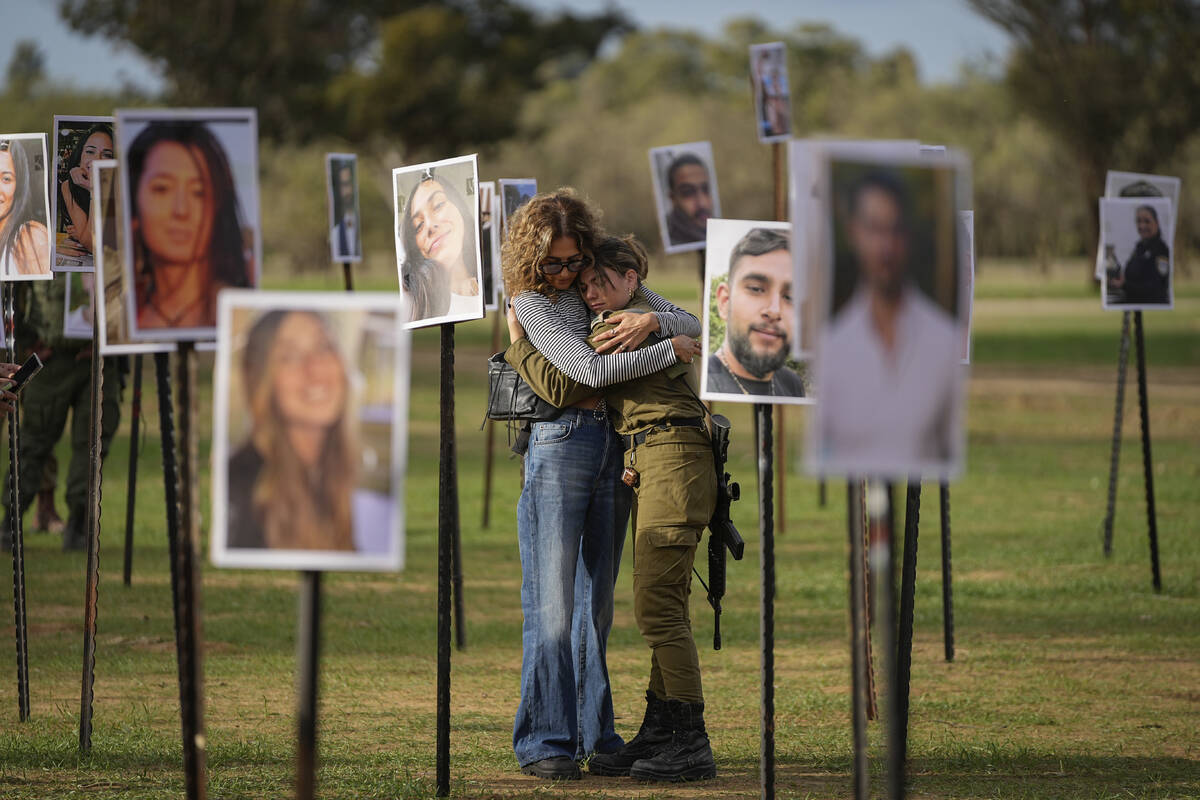 Israelis embrace next to photos of people killed and taken captive by Hamas militants during th ...