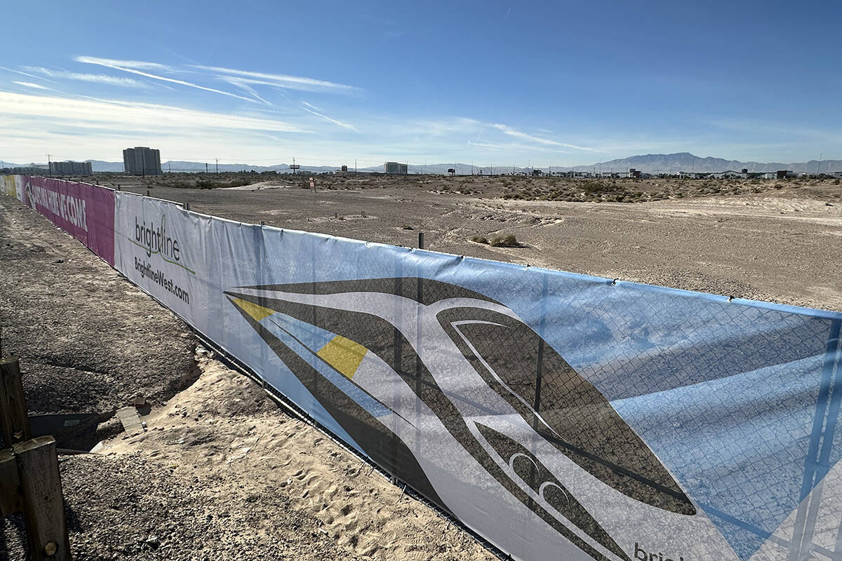 A fence with Brightline West imagery sits on a plot of land where the Las Vegas station of the ...