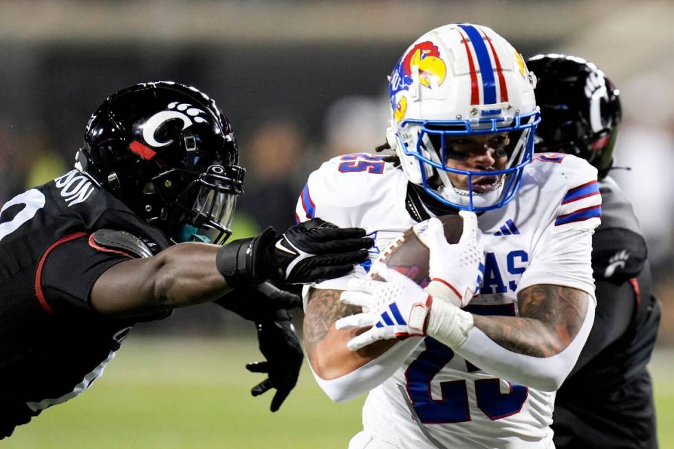 Kansas running back Dylan McDuffie (25) guards the ball from a Cincinnati defender during an NC ...