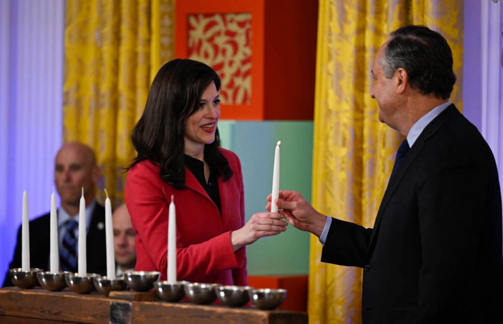 Second gentleman Doug Emhoff passes a Menorah candle to Anne Neuberger at a Hanukkah reception ...