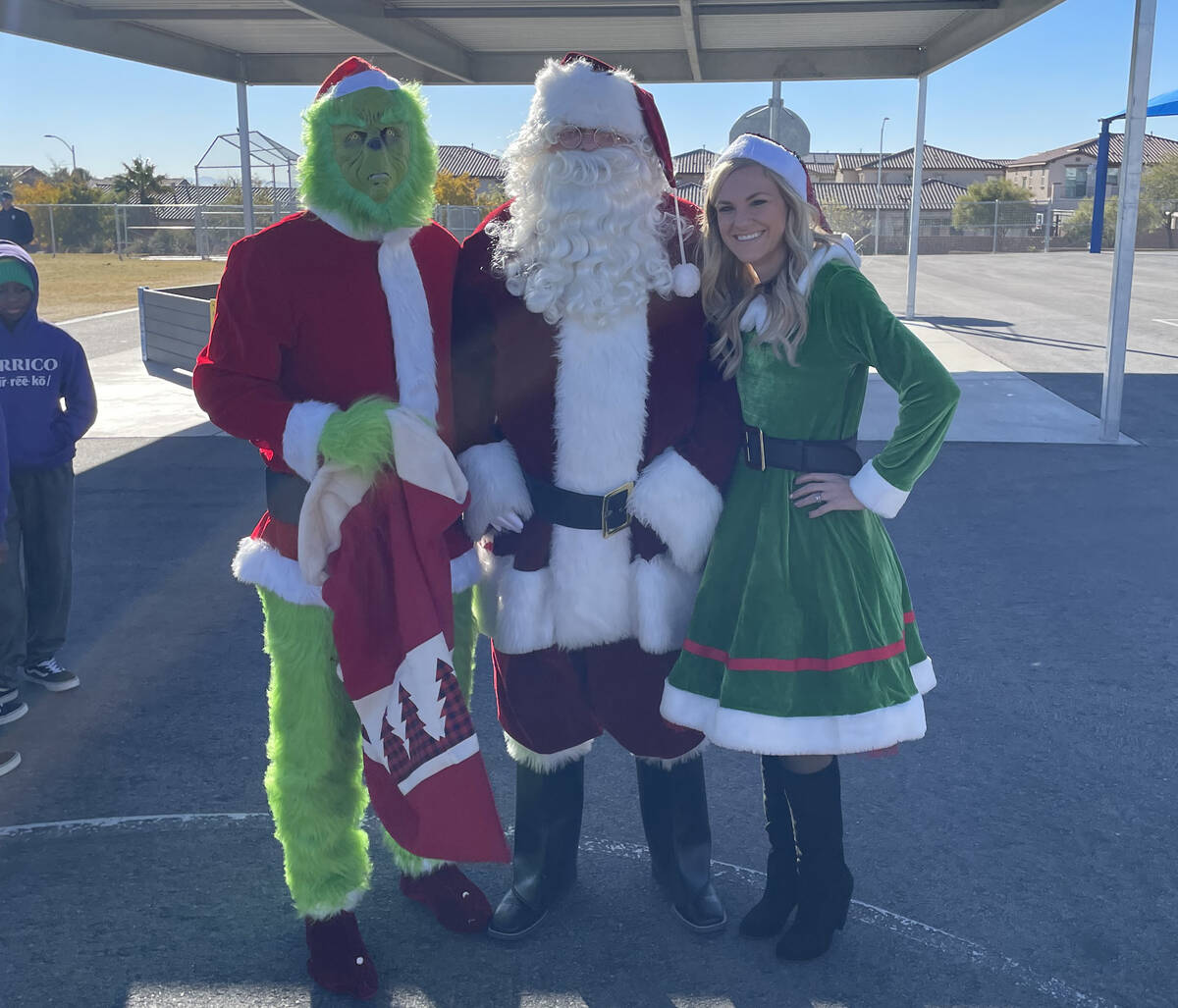 The Grinch, Santa Claus and Mrs. Claus distribute toys to students at Divich Elementary School ...