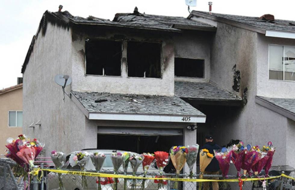 Flowers, stuffed animals and candles are placed on and along a chain-link fence in a makeshift ...