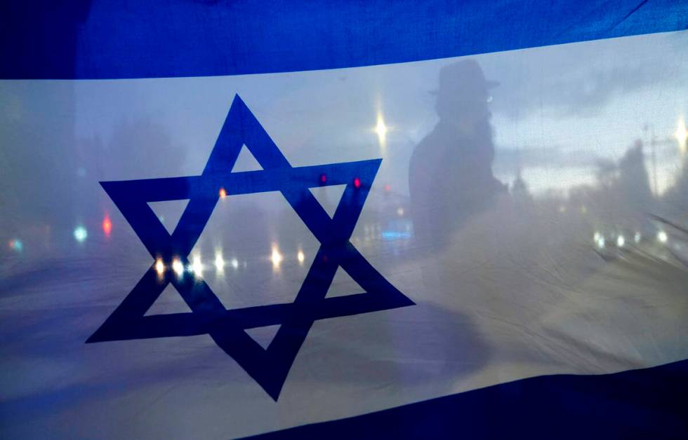 A demonstrator is silhouetted behind a flag of Israel during a rally in support of Israel on Oc ...