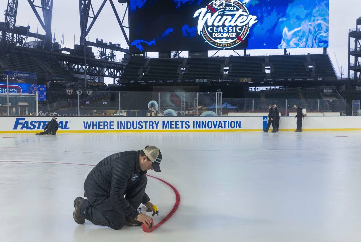A member of the ice crew sprays water on a line so it will stay in place on the skating rink at ...