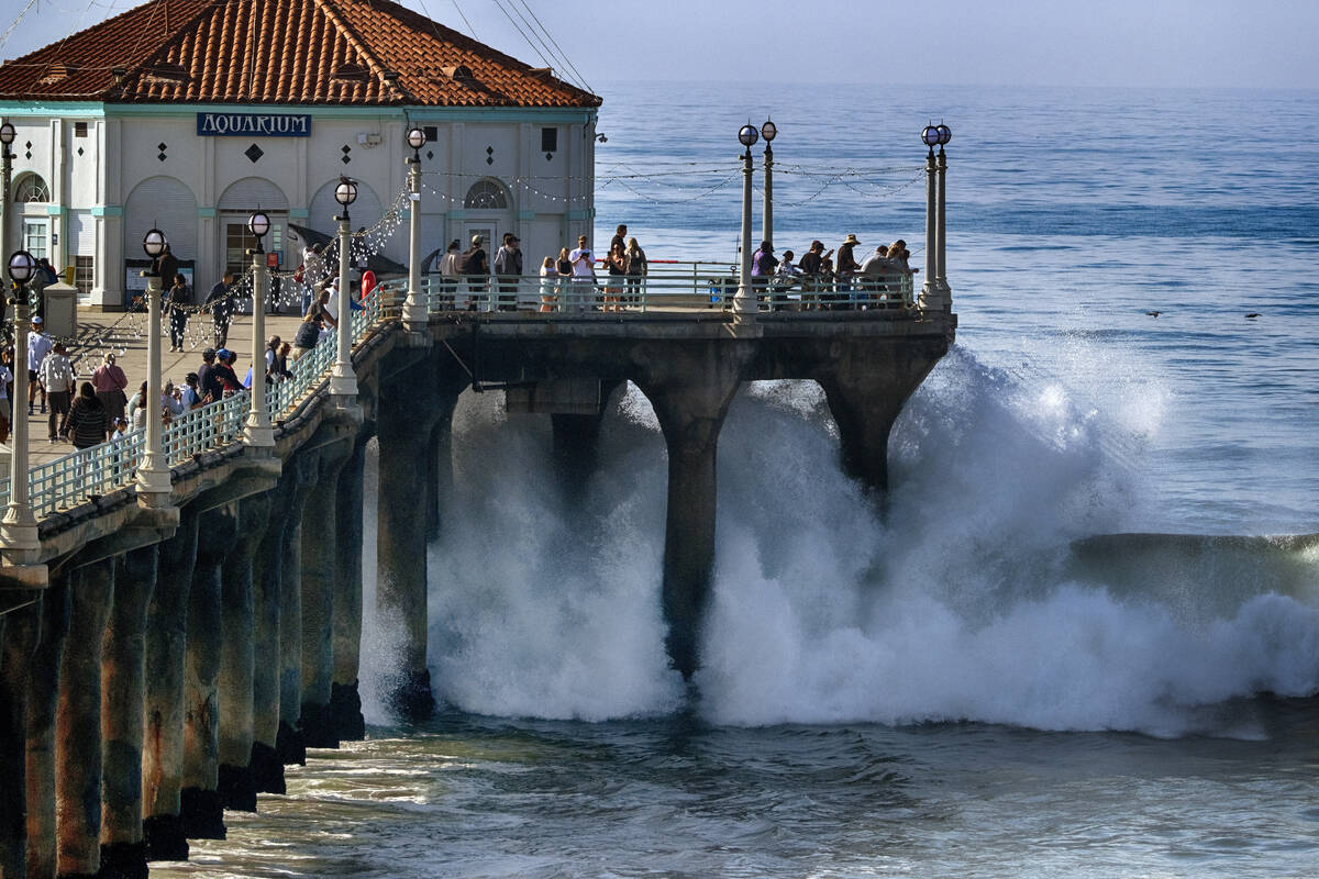 People watch as turbulent surf pounds the side of the pier in Manhattan Beach, Calif. on Thursd ...