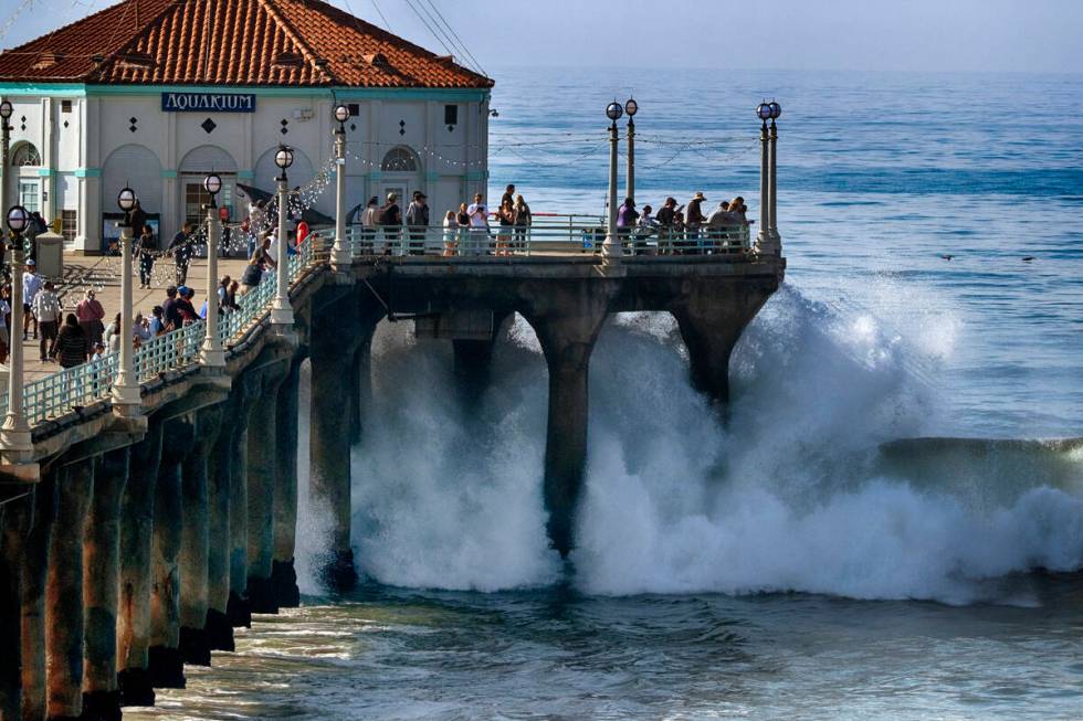People watch as turbulent surf pounds the side of the pier in Manhattan Beach, Calif. on Thursd ...