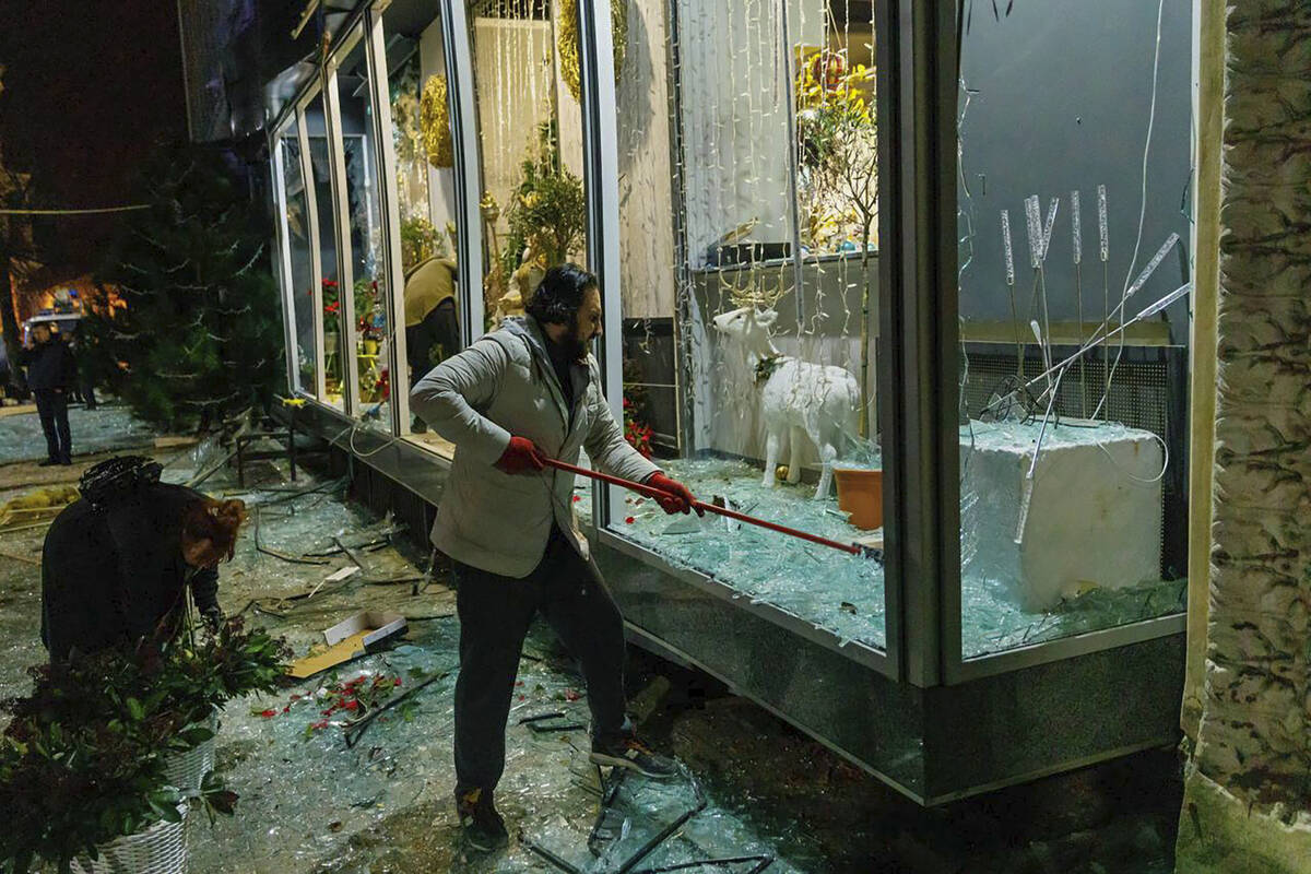In this photo provided by Kharkiv Regional Administration, a man clears broken glass in a store ...
