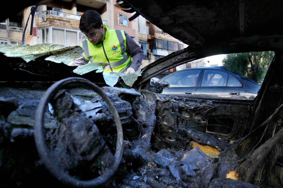 A Hezbollah Civil defense worker searches for body remains on a burned car, near an apartment b ...