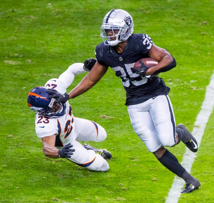 Raiders running back Zamir White (35) stiff arms Denver Broncos cornerback Fabian Moreau (23) o ...