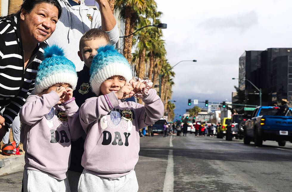 Twin sisters Ava and Anaya Pedraza, 2, make heart shapes with their hands as floats passing by ...