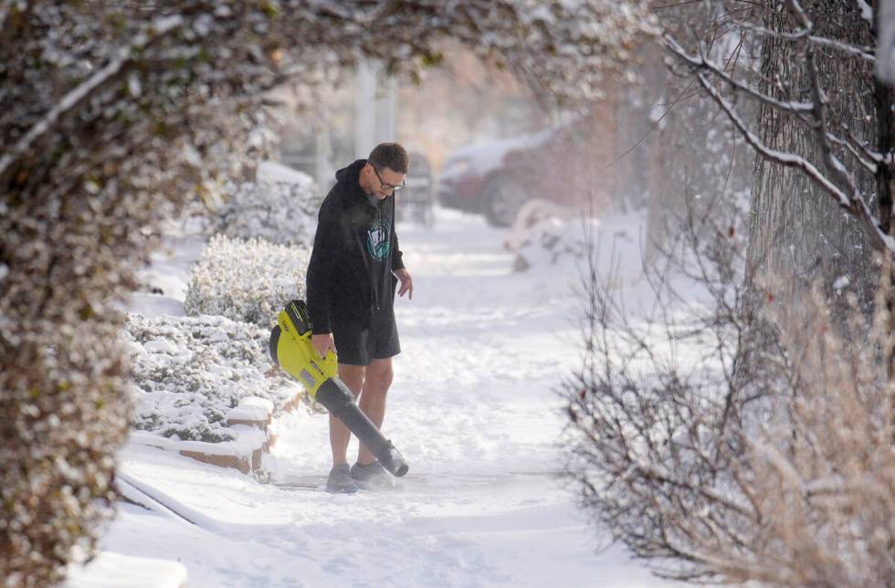 With the daytime high temperature far below zero, a man uses a leaf blower to clear a light sno ...