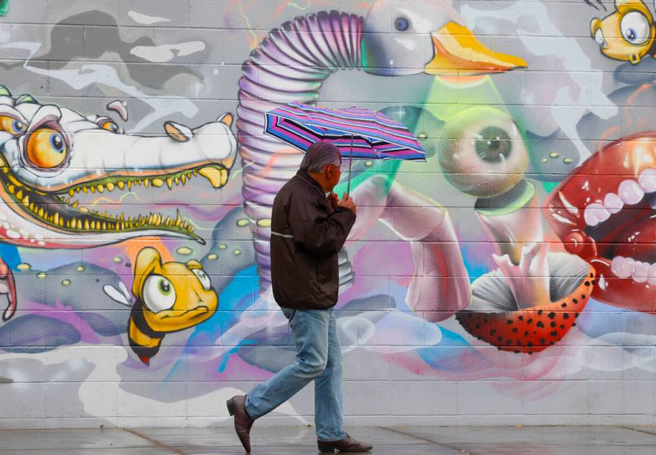 A pedestrian holding un umbrella walks past a mural on Third Street during a rainy morning, on ...