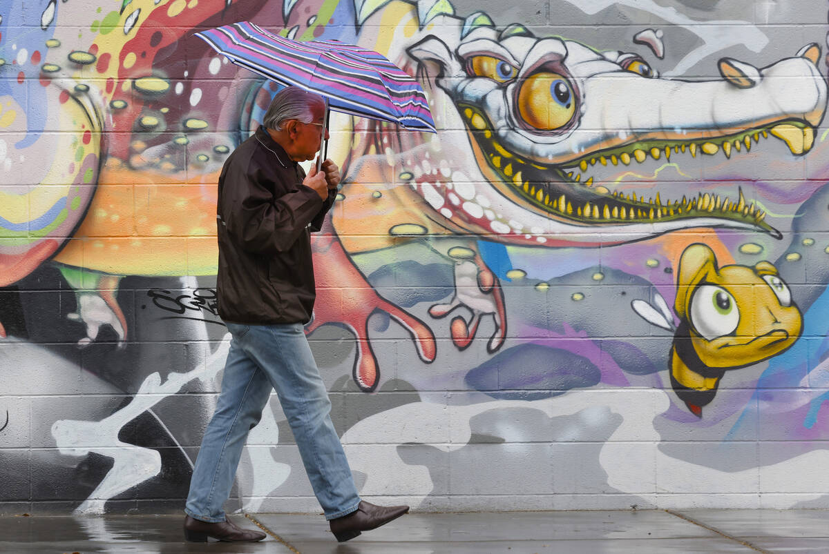 A pedestrian holding un umbrella walks past a mural on Third Street during a rainy morning, on ...