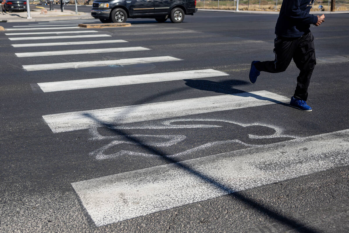 A pedestrian crosses chalk outlines freshly painted by the Las Vegas Fire Department at the int ...