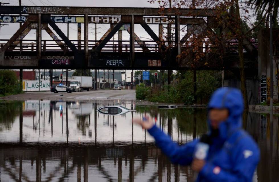 A television reporter does a broadcast as cars are seen submerged on a flooded street under a r ...