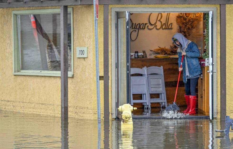 A worker at Sugar Bella sweeps flood waters out the front door on Marina Drive, just south of P ...