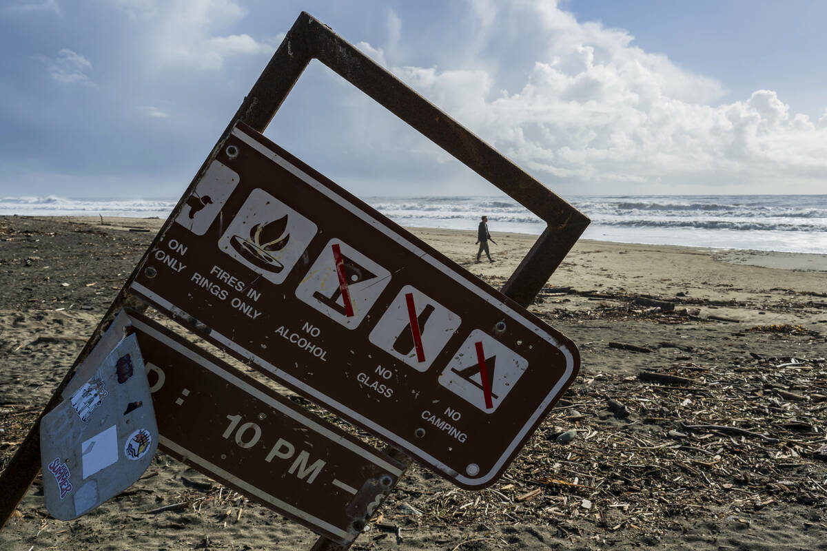 A man walks along Rio Del Mar beach near a sign damaged in recent storms Thursday, Feb. 1, 2024 ...