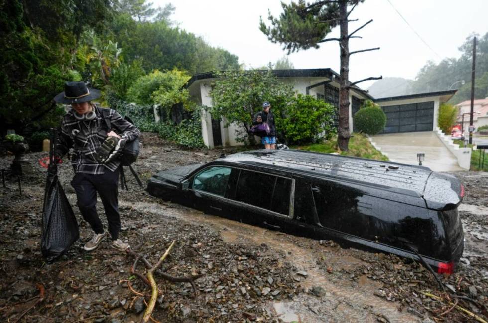 Residents evacuate past damaged vehicles after storms caused a mudslide, Monday, Feb. 5, 2024, ...