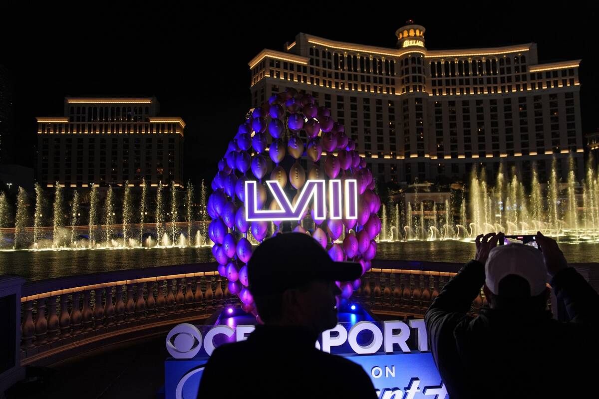 People stand by signage for the Super Bowl as the Bellagio fountains erupt along the Las Vegas ...