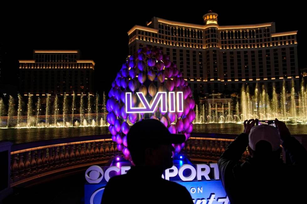 People stand by signage for the Super Bowl as the Bellagio fountains erupt along the Las Vegas ...