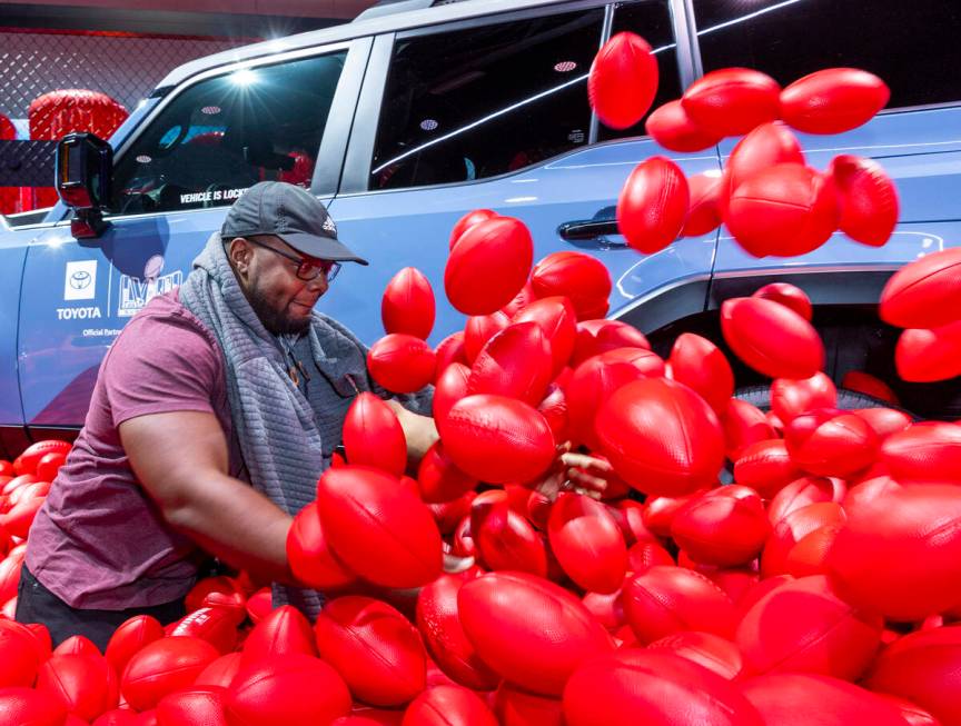 Julian Walker of Los Angeles digs through a pit of footballs looking for a hidden prize for the ...