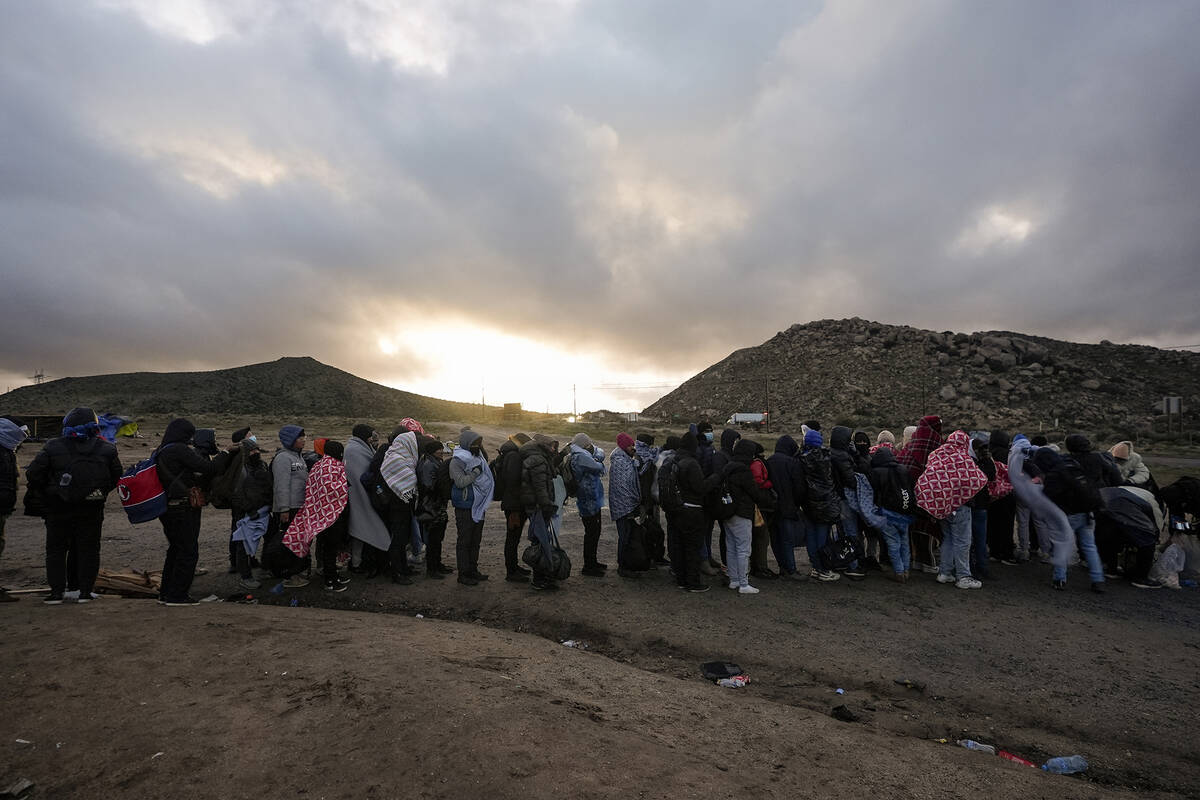 Asylum-seeking migrants line up in a makeshift, mountainous campsite to be processed after cros ...