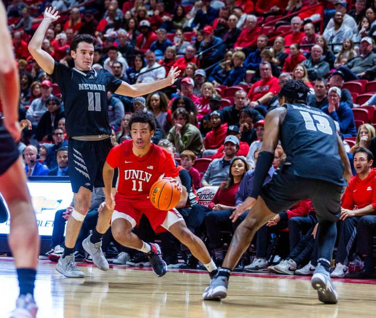 UNLV Rebels guard Dedan Thomas Jr. (11) cuts between UNR forward Nick Davidson (11) and Kenan B ...