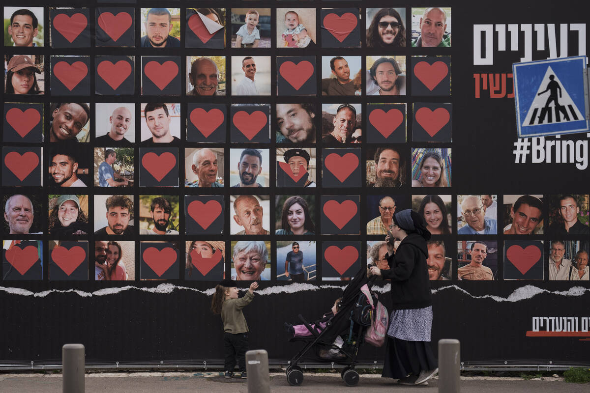 FILE - A woman and her children walk past a wall with photographs of hostages who were kidnappe ...