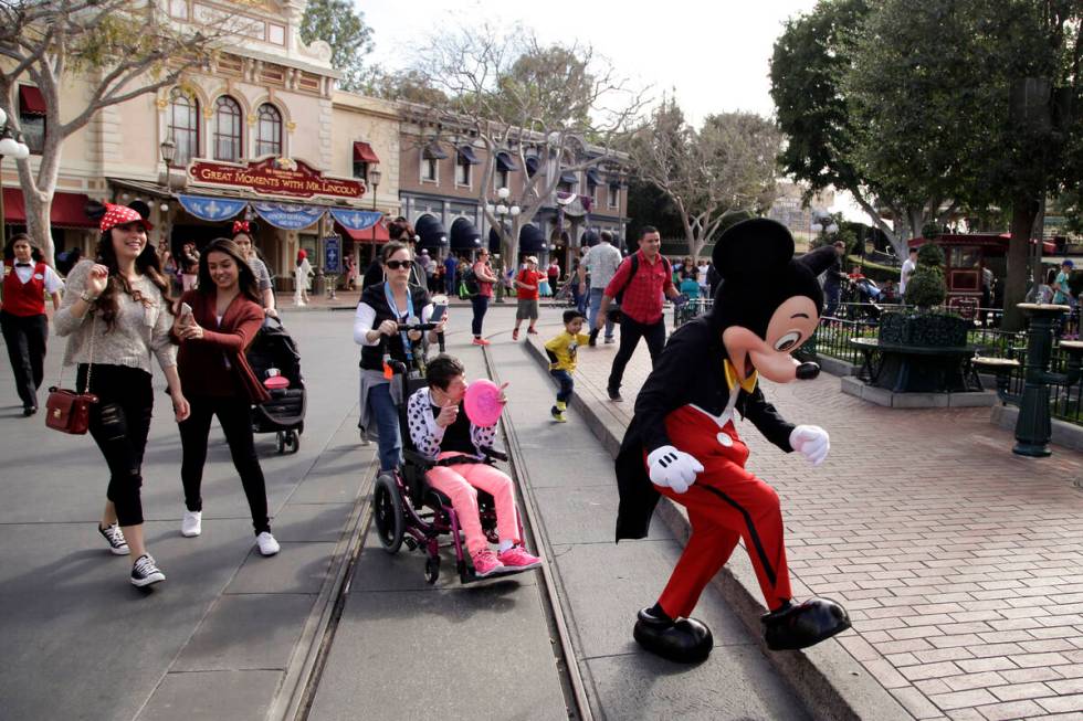 Visitors follow Mickey Mouse for photos at Disneyland, Jan. 22, 2015, in Anaheim, Calif. Disney ...