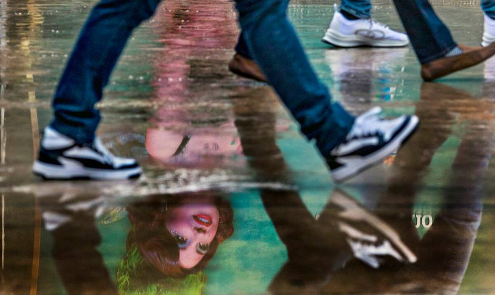 The Green Fairy from the show Absinthe is reflected in a puddle as pedestrians walk past the en ...