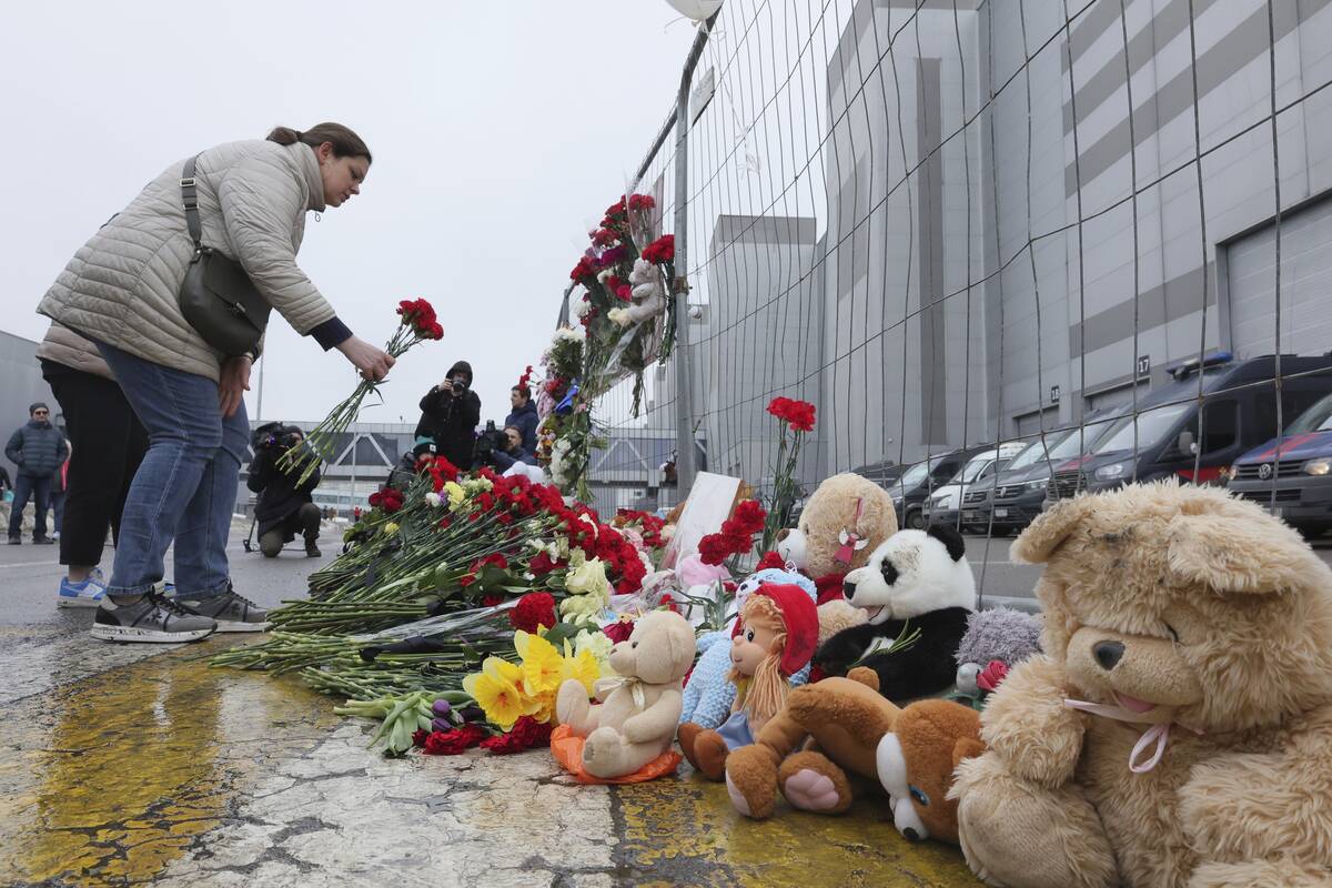 A woman places flowers by the fence next to the Crocus City Hall, on the western edge of Moscow ...