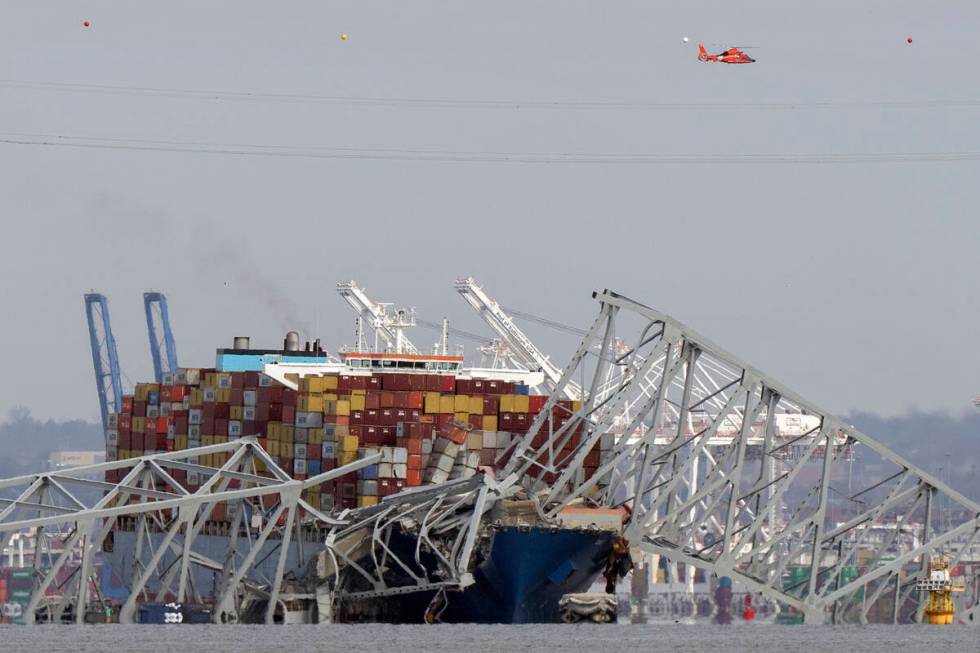 A helicopter flies over a container ship as it rests against wreckage of the Francis Scott Key ...