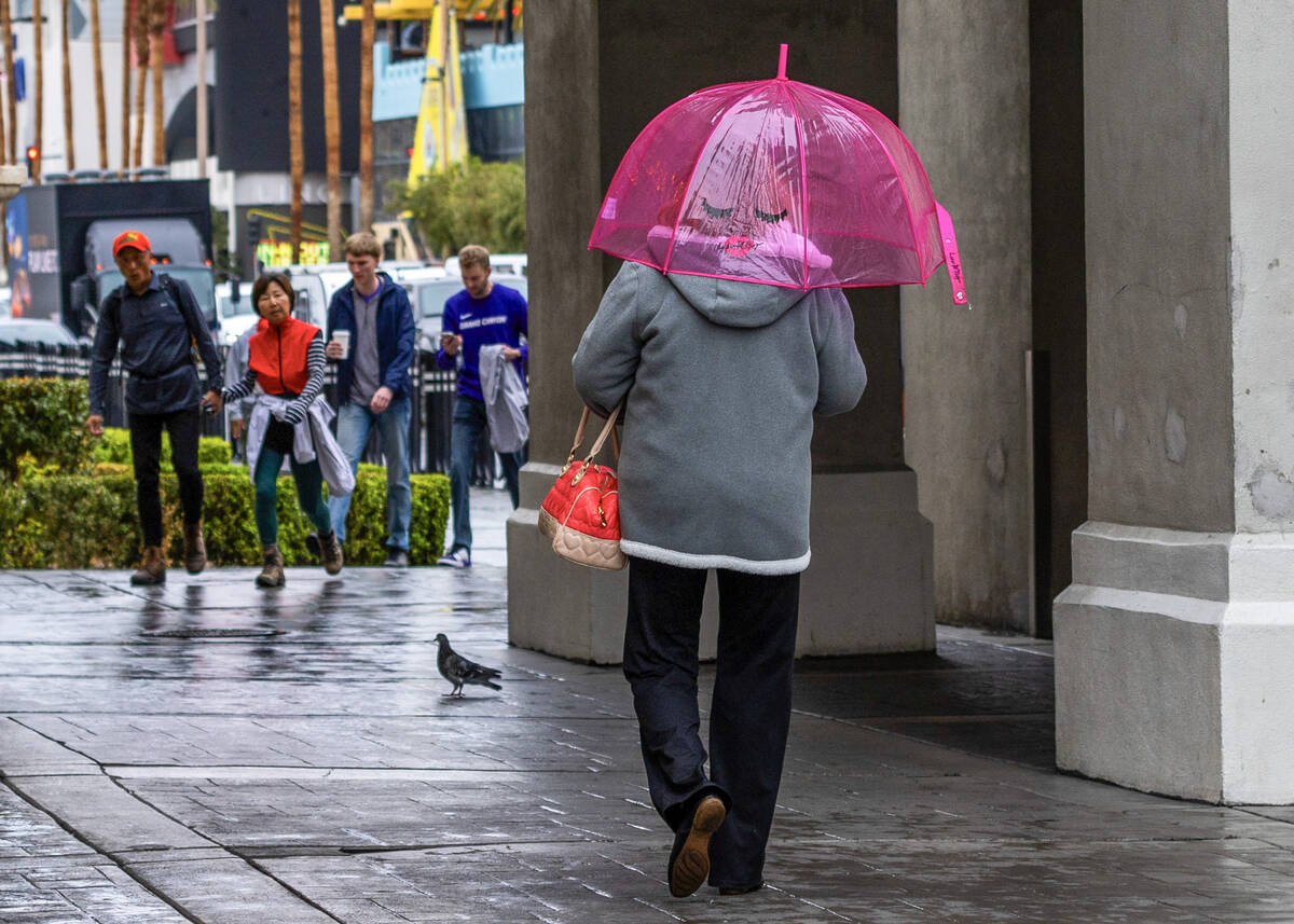 A woman walks with a fun umbrella along the Strip near Caesars Palace during a rainy day on Fri ...