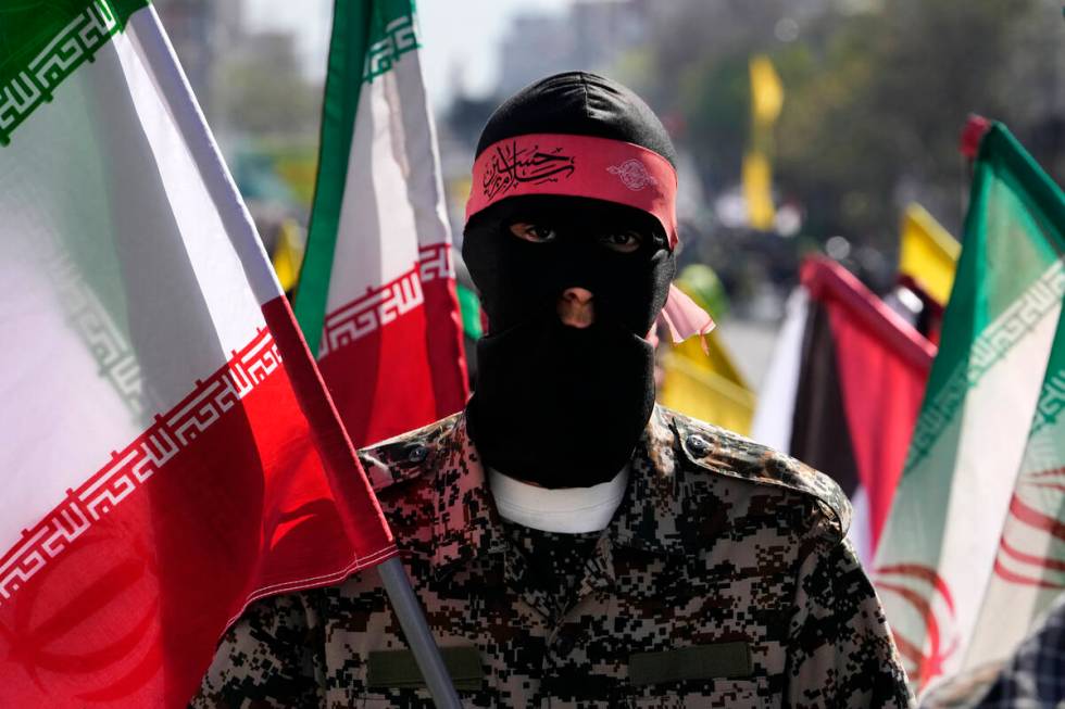 A member of the Iranian paramilitary Basij force holds an Iranian flag as he covers her face in ...