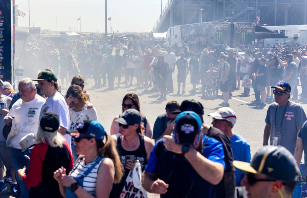 Fans cover up as nitromethane from a top fuel dragster fill the air in the pits during Day 1 of ...