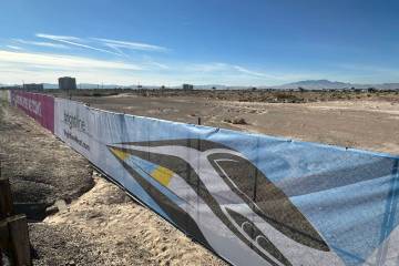 A fence with Brightline West imagery sits on a plot of land where the Las Vegas station of the ...