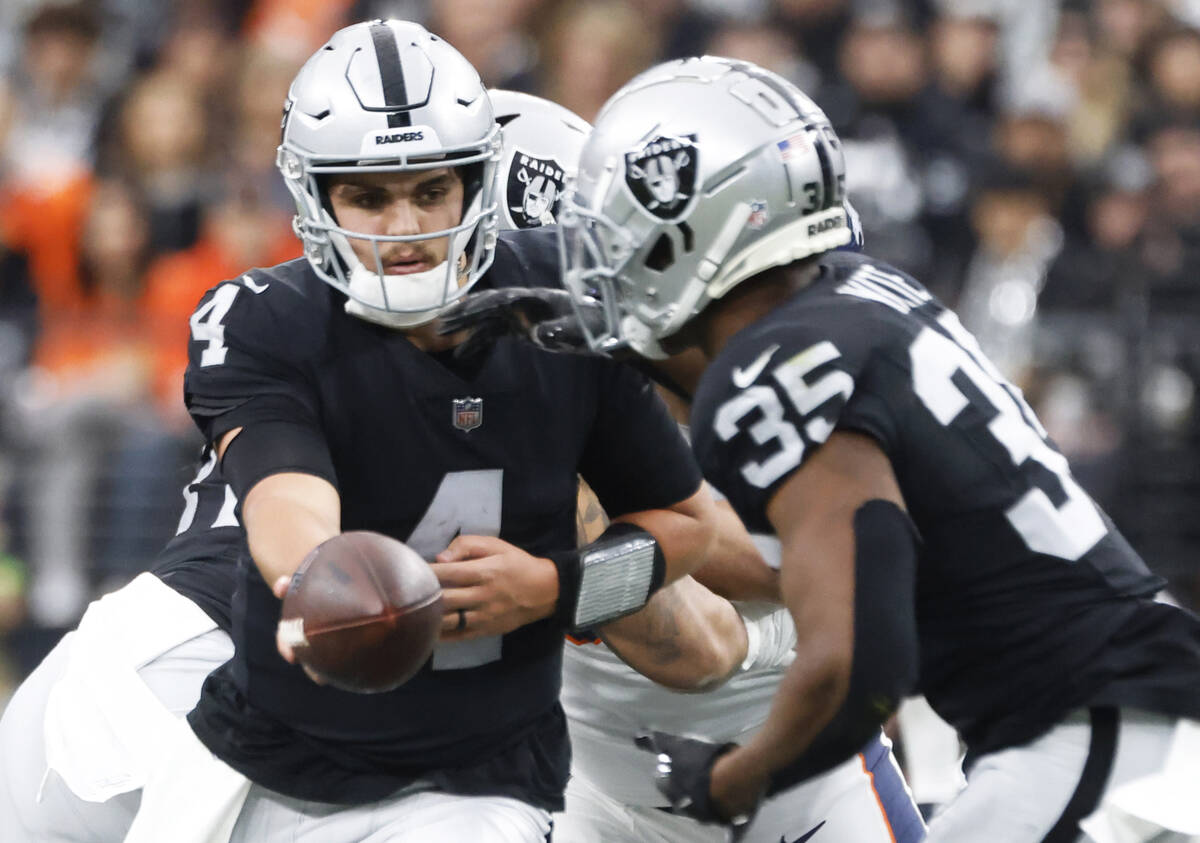 Raiders quarterback Aidan O'Connell (4) hands off to Raiders running back Zamir White (35) duri ...