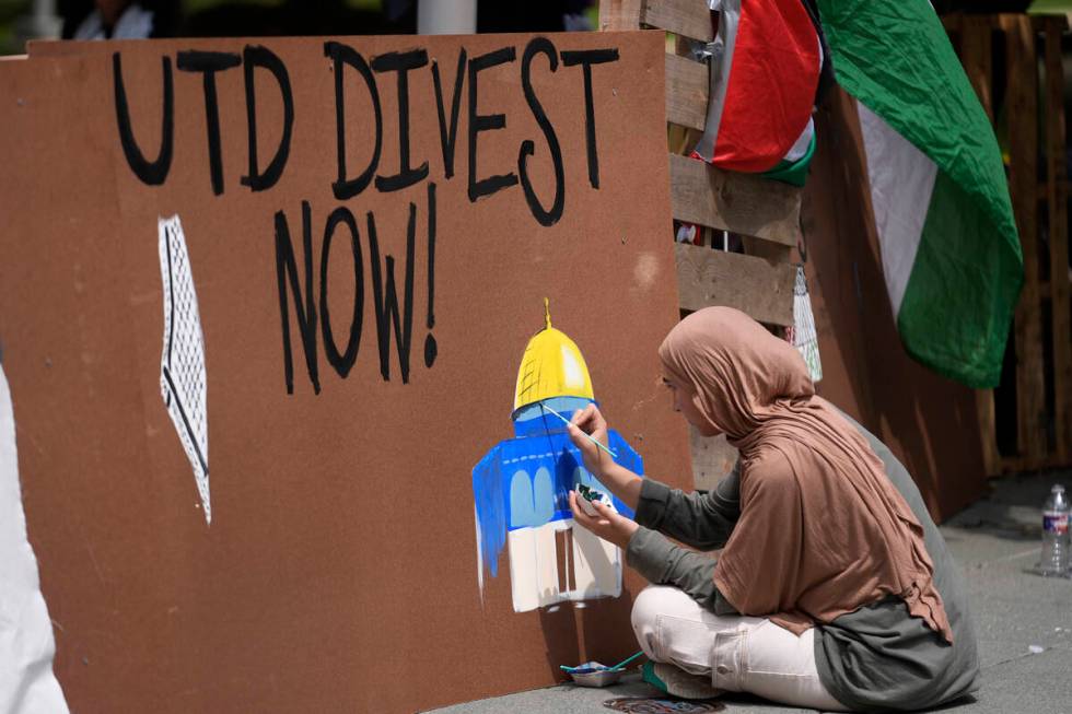 A woman paints on a barrier during a protest set up in a plaza at the University of Texas at Da ...