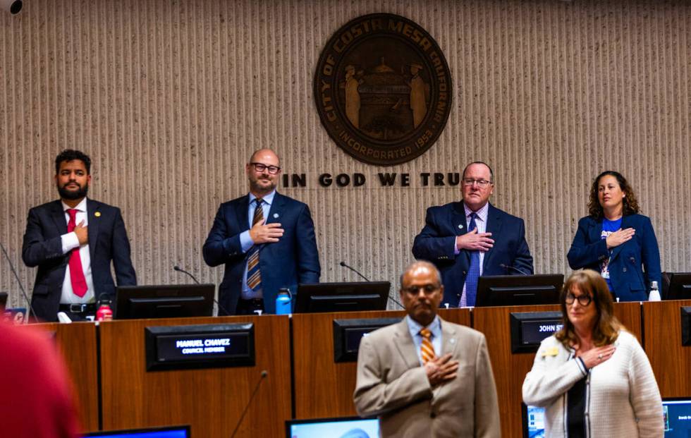 City of Costa Mesa council members stand for the Pledge of Allegiance opening their meeting to ...