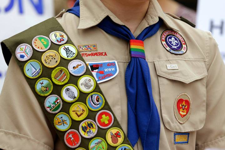 Merit badges and a rainbow-colored neckerchief slider are affixed on a Boy Scout uniform outsid ...