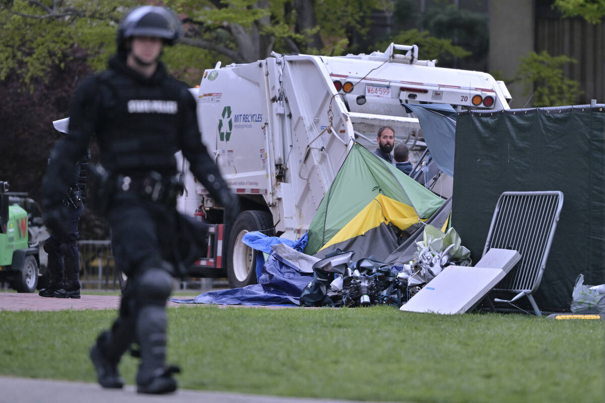 A police officer in riot gear walks past a garbage truck being loaded with the remains of the p ...