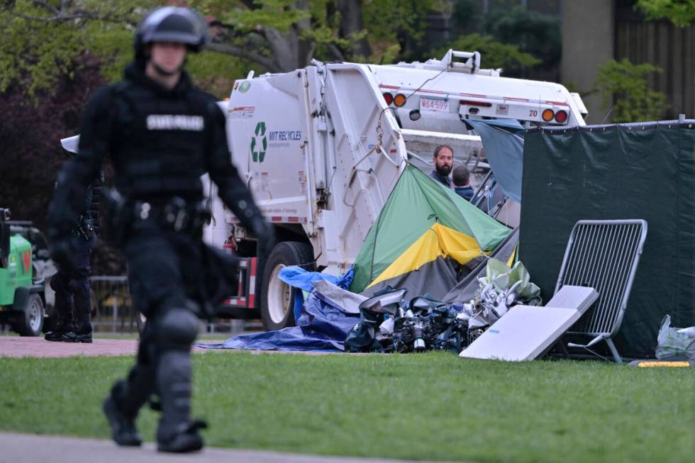 A police officer in riot gear walks past a garbage truck being loaded with the remains of the p ...