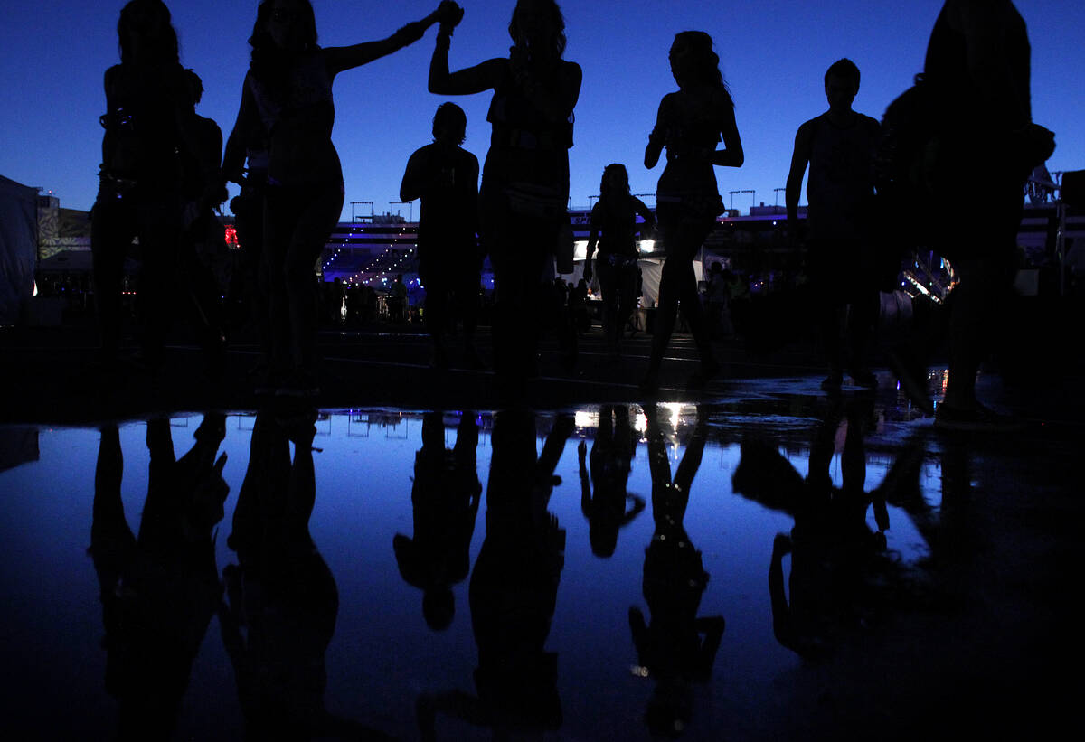 People are reflected in a puddle as they attend the Electric Daisy Carnival at the Las Vegas Mo ...