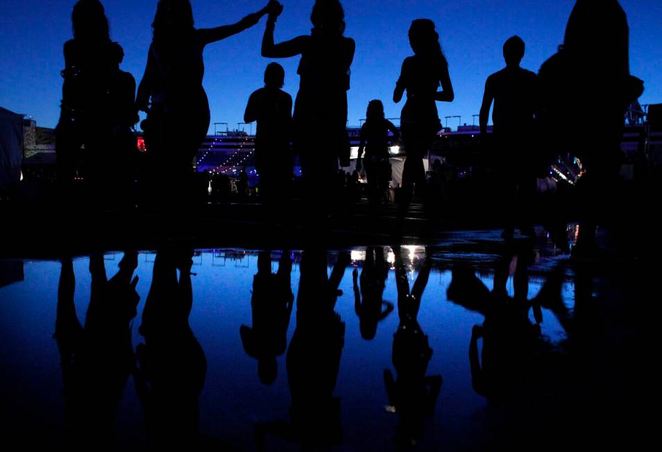 People are reflected in a puddle as they attend the Electric Daisy Carnival at the Las Vegas Mo ...