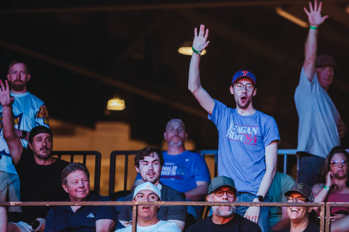 Fans in the audience cheer to get a free t-shirt during a professional cornhole matchup between ...