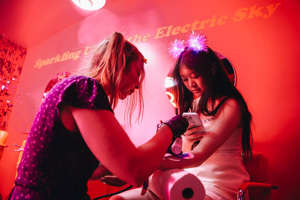 A festival attendee receives an airbrush tattoo inside of a Dunkin’ Donuts themed pop up ...